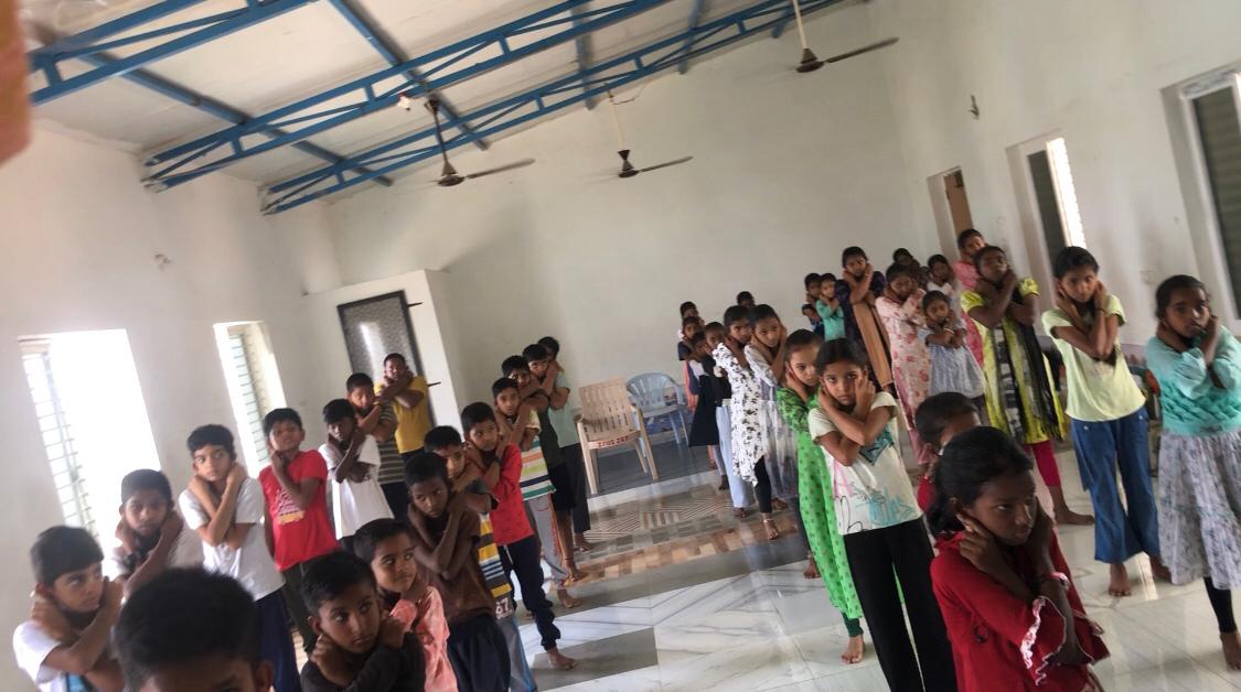 Positioning of fingers on earlobes during Super Brain Yoga at Summer Camp, P.M. Sri Zilla Parishad High School, Jakranpally, Nizamabad Dist.