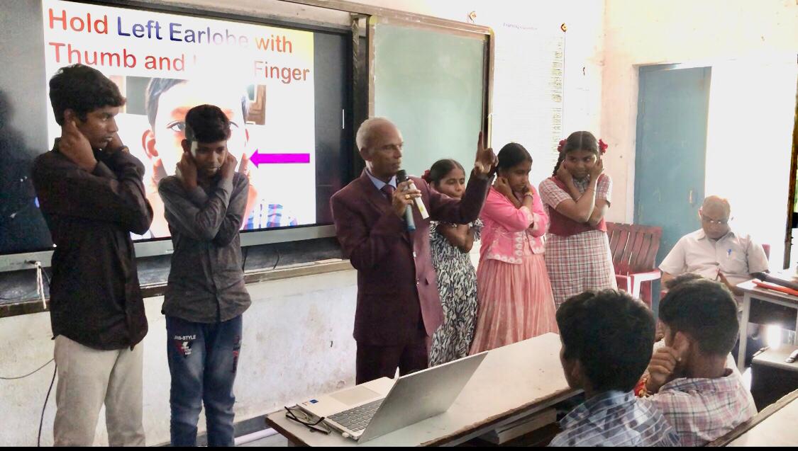 Demonstration of positioning of fingers on earlobes - Workshop on  Super Brain Yoga at Zilla Parishad High School, Gopalpet, Nagireddy Pet Mandal sponsored by International  Lions Club of Nizamabad-Netha.